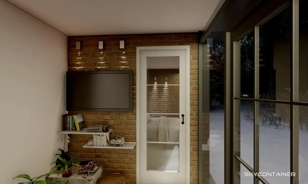 Container home interior with a television on a brick wall beside the kitchen