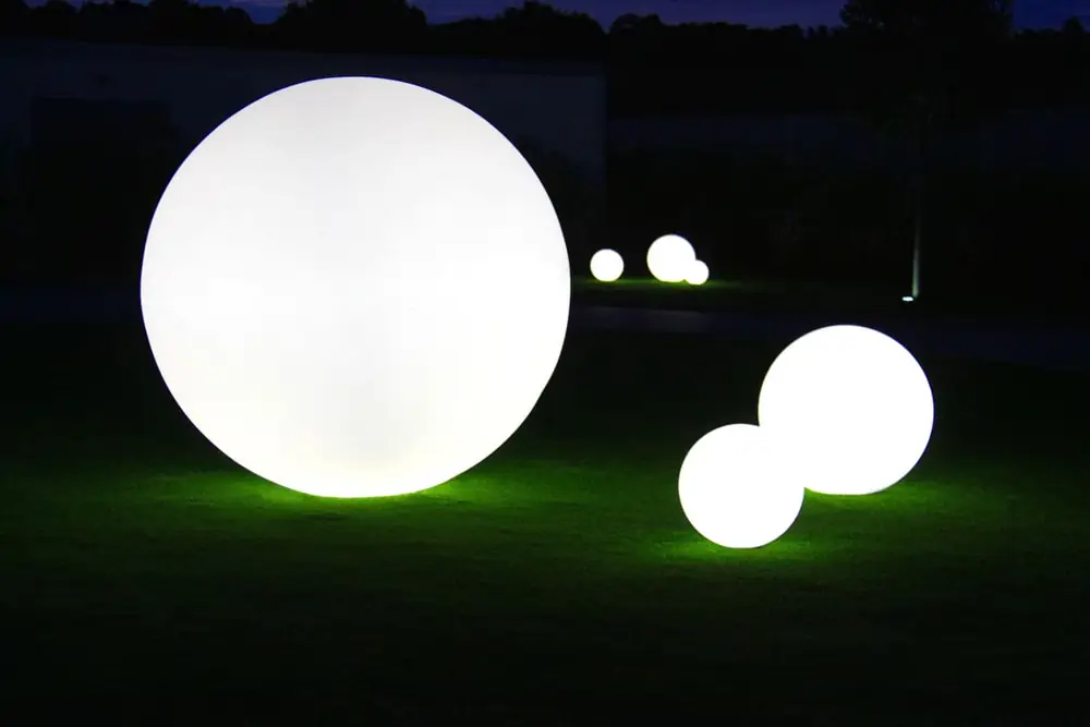 Leuchtende Kugeln in verschiedenen Größen im Garten bei Nacht