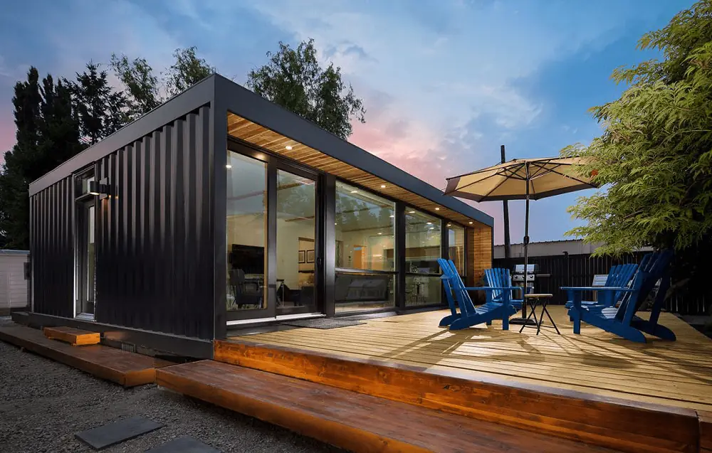 Dark tiny garden house with a timber deck, parasol and blue chairs