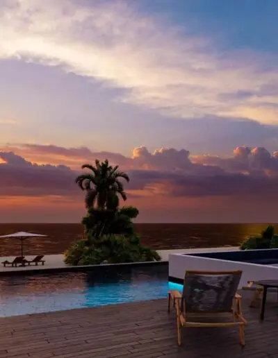 Poolkante und Terrassenmöbel vor dem Meer bei orangefarbenem Abendhimmel