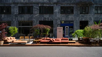 Fast Via Durini 2026: Street-side terrace with warm upholstery, plants and different table surfaces · View 1