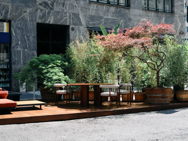 Fast Via Durini 2026: Street-side terrace with warm upholstery, plants and different table surfaces · View 2