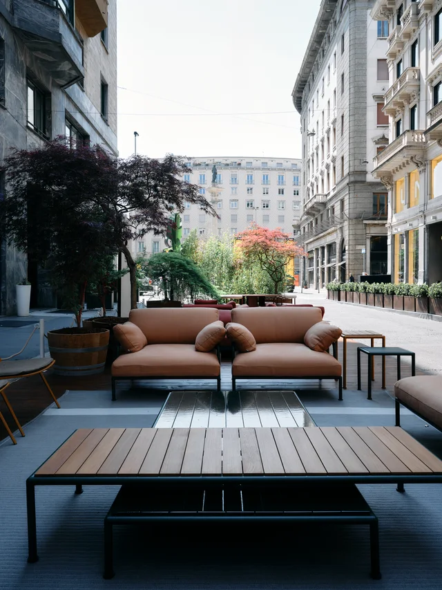Fast Via Durini 2026: Street-side terrace with warm upholstery, plants and different table surfaces · View 3