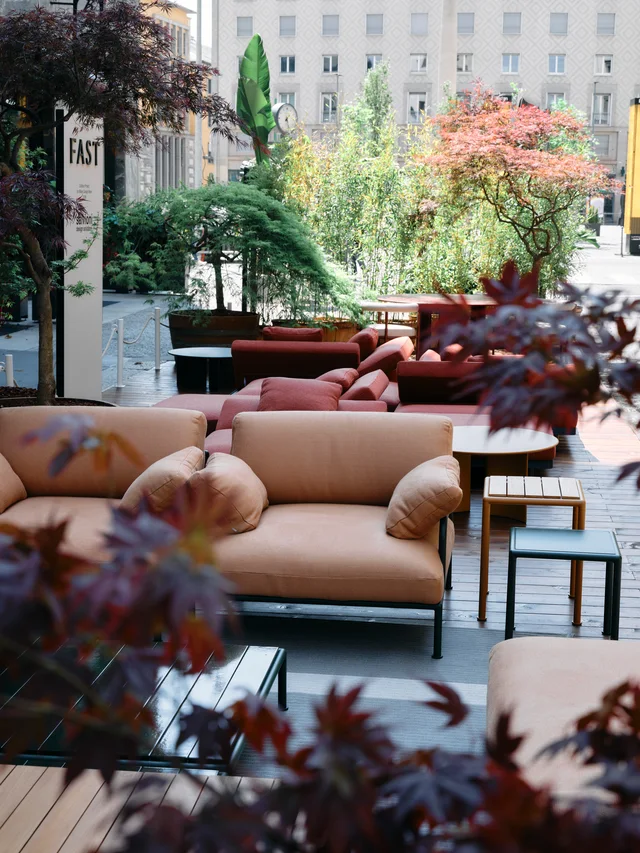 Fast Via Durini 2026: Street-side terrace with warm upholstery, plants and different table surfaces · View 4