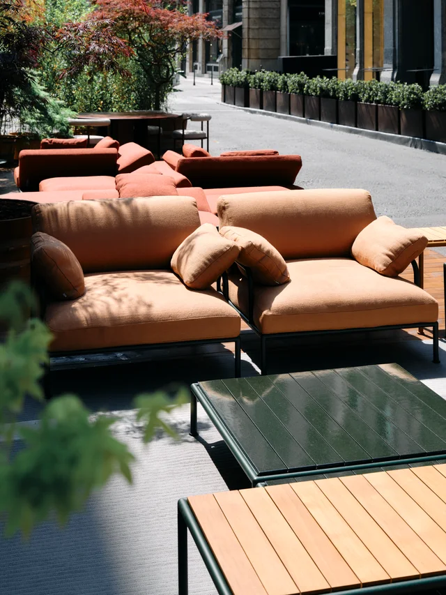 Fast Via Durini 2026: Street-side terrace with warm upholstery, plants and different table surfaces · View 5