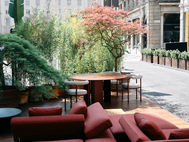 Fast Via Durini 2026: Street-side terrace with warm upholstery, plants and different table surfaces · View 20