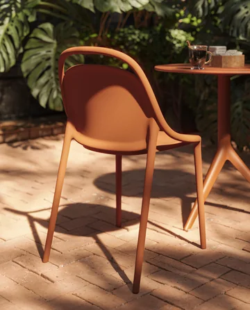 VONDOM B2B: orangefarbener Stuhl schräg neben einem runden Tisch und Pflanzen