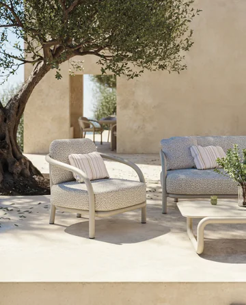 VONDOM GUM: heller Sessel mit gebogenem Rohrrahmen neben einem Sofa und Olivenbaum